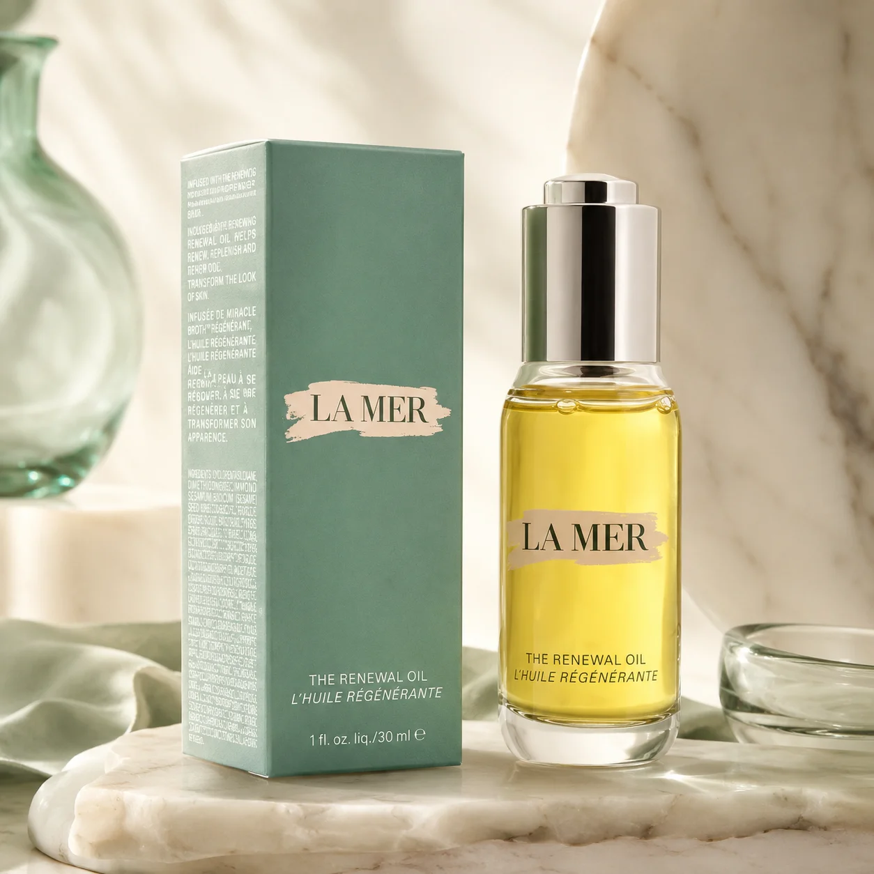 A bottle of La Mer The Renewal Oil with its green packaging box set on a marble surface and soft background lighting.